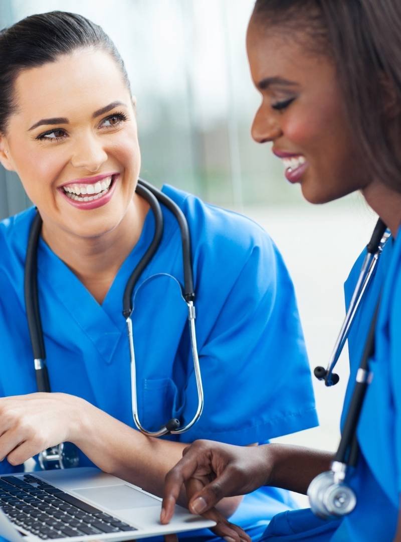Two nurses smiling while working on a laptop